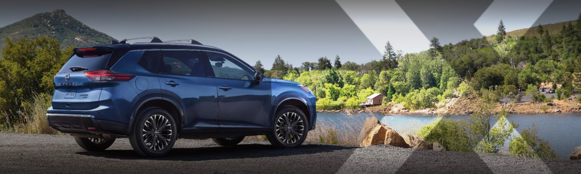 nexauto : Nissan Rogue bleu vu de côté devant un cours d'eau avec une montagne en arrière plan.